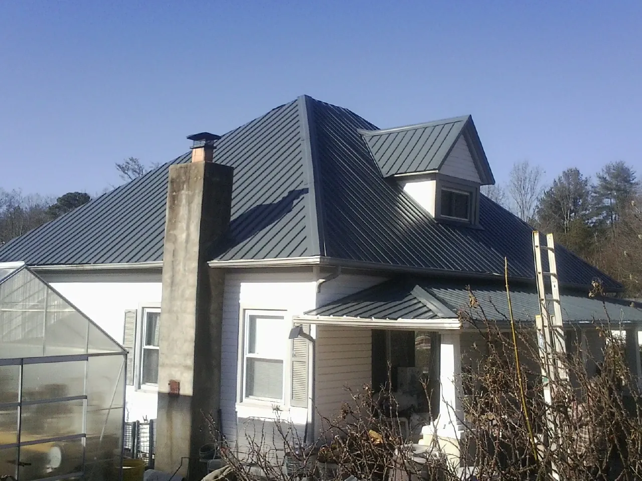 Dark blue standing seam metal roof on a white farmhouse with dormer — Slate & Tile Roof Repair by Roofing Brothers in Lucas