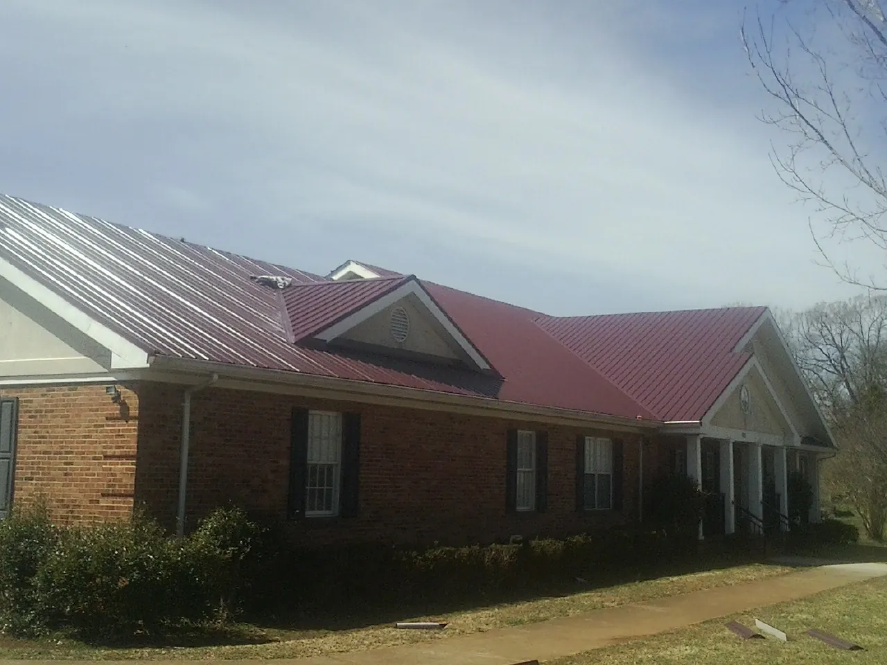Red metal roof with gabled entries on a long brick building, from a Hail Damage Roof Repair job in Lucas